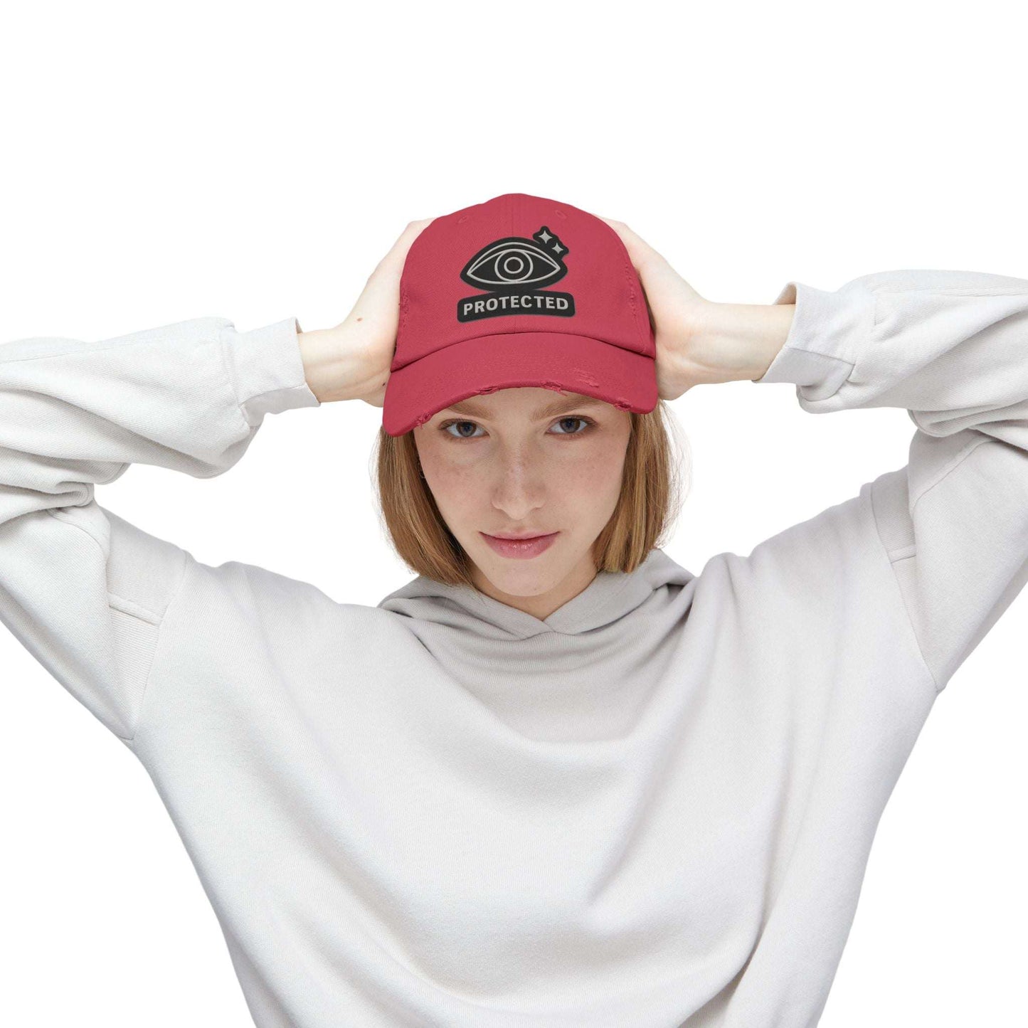 Red Protected Eye Distressed Dad Hat worn by woman in white hoodie. Embroidered eye symbol on vintage-style unisex cap.