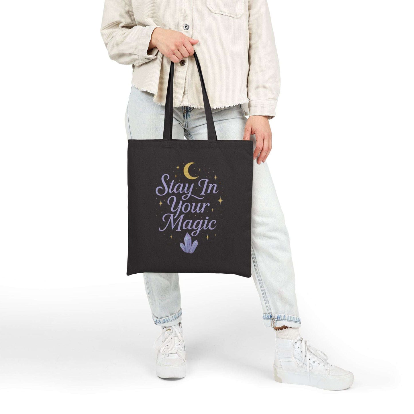Black tote bag with motivational quote 'Stay In Your Magic', held in hand against a neutral background, modern aesthetic.