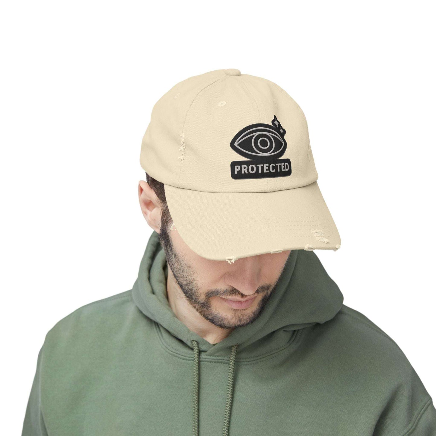 Beige Protected Eye Distressed Dad Hat worn by man in green hoodie. Embroidered eye graphic on frayed-edge unisex cap.