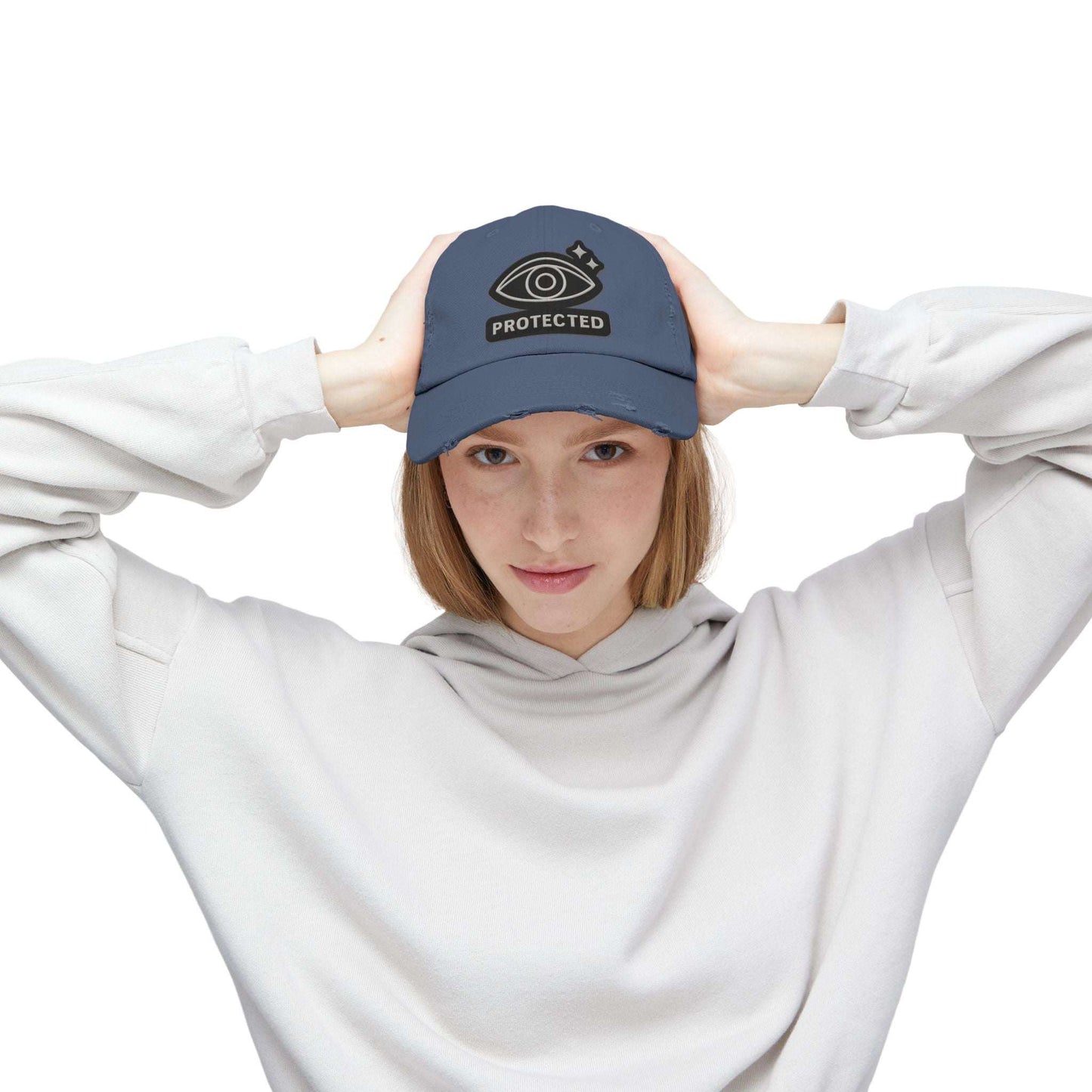 Blue Protected Eye Distressed Dad Hat worn by woman in white hoodie. Embroidered eye graphic on vintage-style unisex cap.