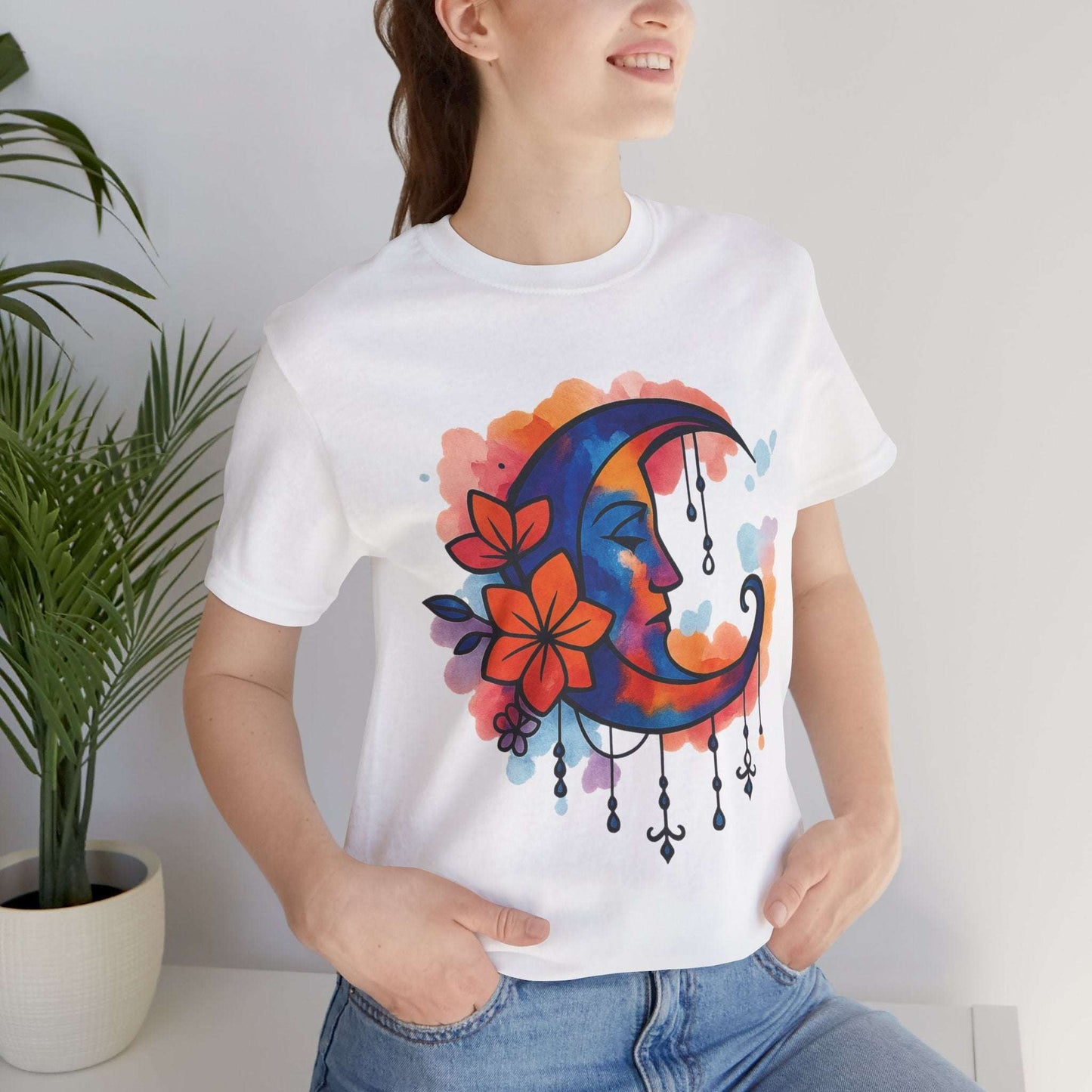 White Floral Moonface Goddess Tee featuring a colorful boho crescent moon with floral accents and charms, ideal for spiritual and festival wear.