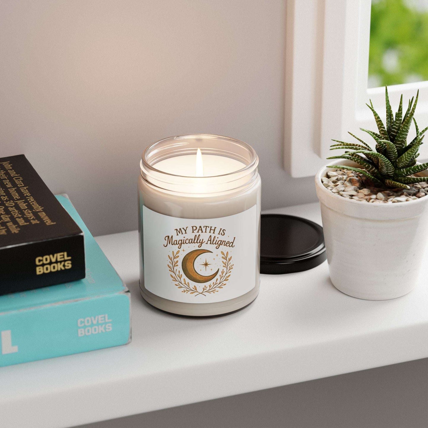 Magically Aligned 9oz Soy Candle — Moon & Stars Scented Jar glowing on a windowsill beside books and a succulent, enhancing relaxation and meditation spaces.