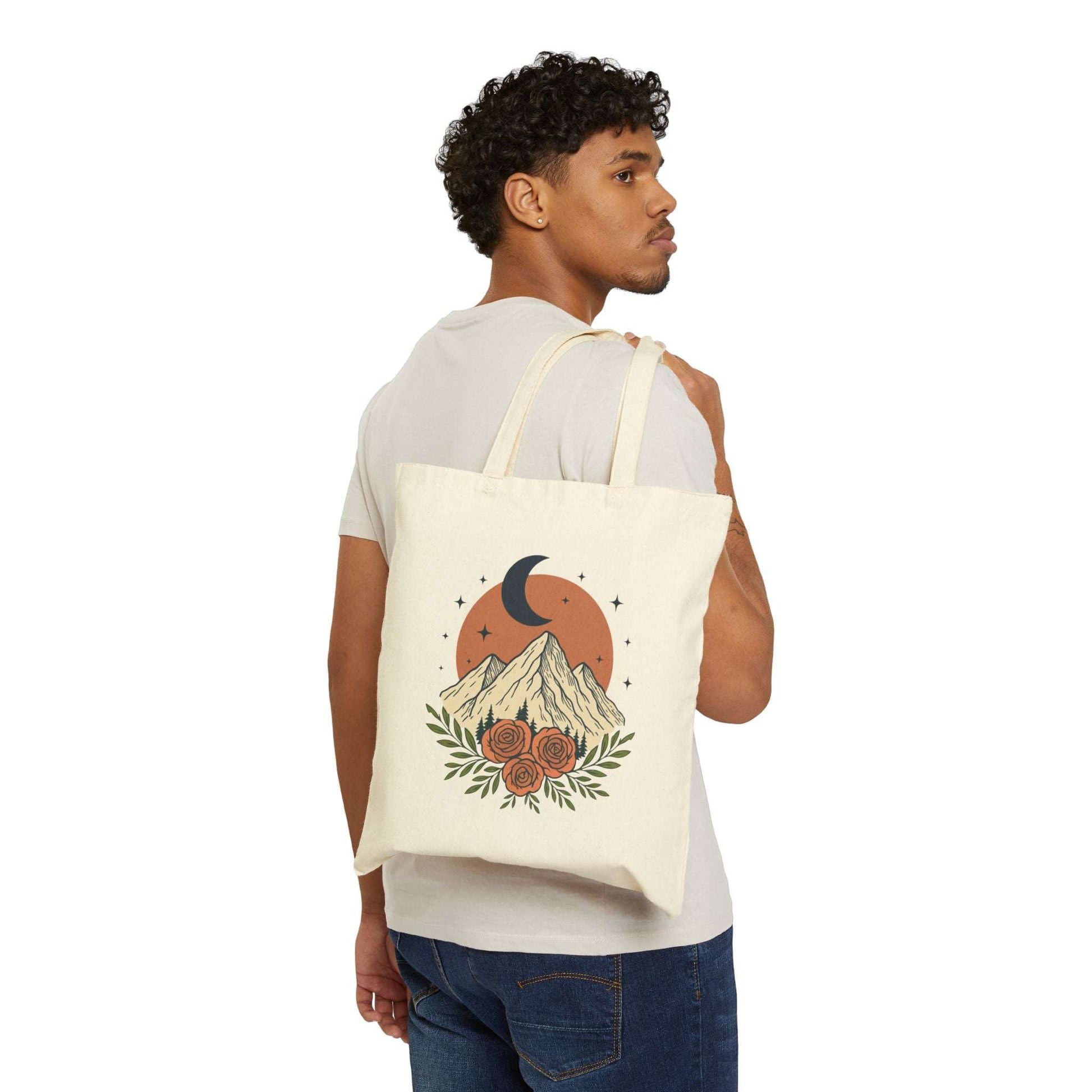 Man carrying canvas tote bag with moon, mountain, and rose print. Durable eco shopper ideal for books, groceries, or outdoor essentials.