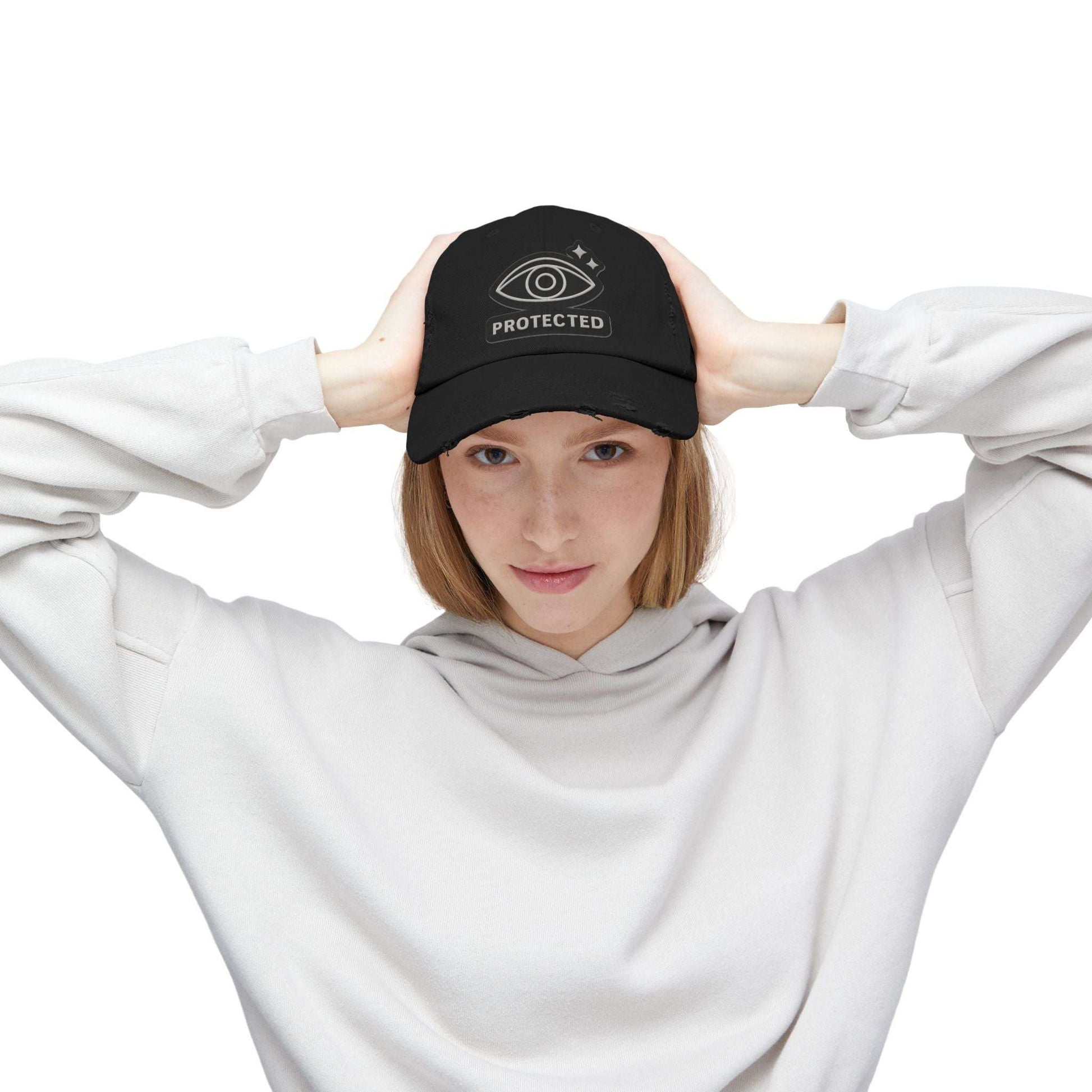 Black Protected Eye Distressed Dad Hat worn by woman in white hoodie. Embroidered eye design on vintage-style unisex cap.