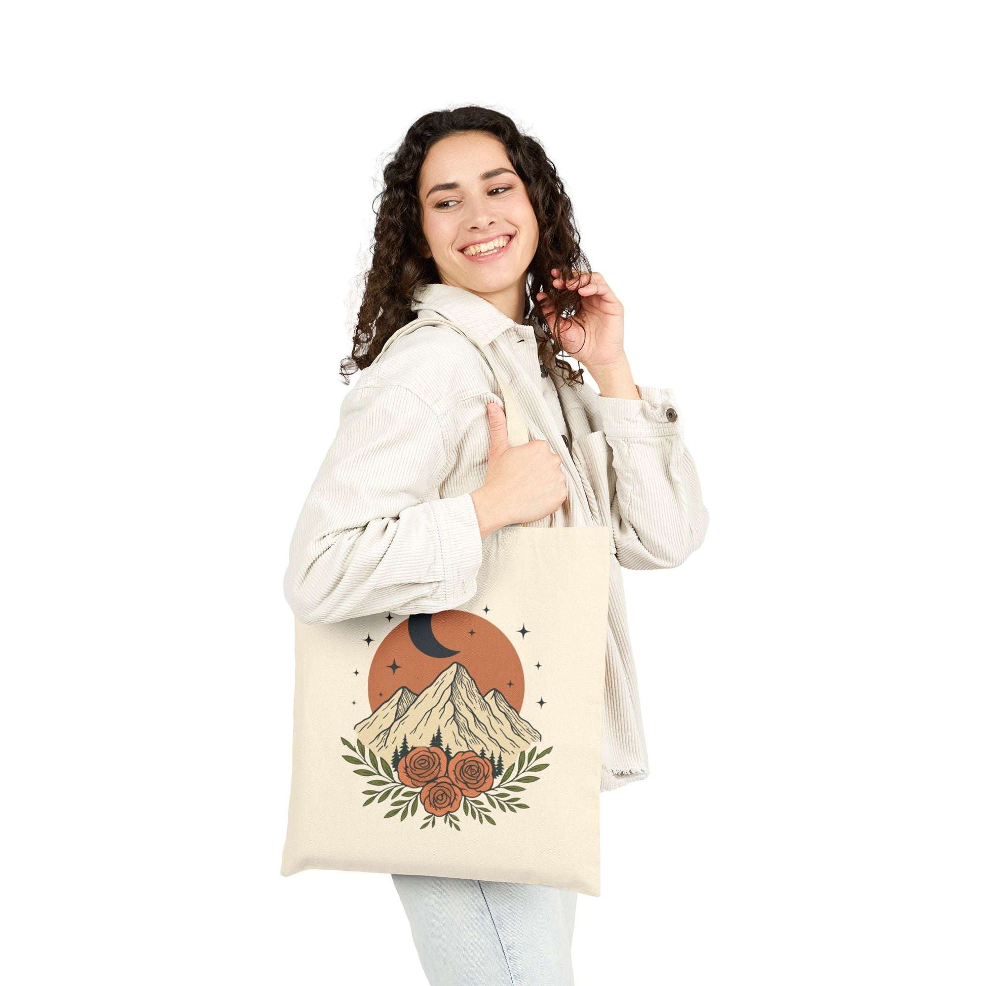 Woman holding canvas tote bag with vintage moon and rose mountain design. Boho eco-friendly tote for shopping or everyday carry.