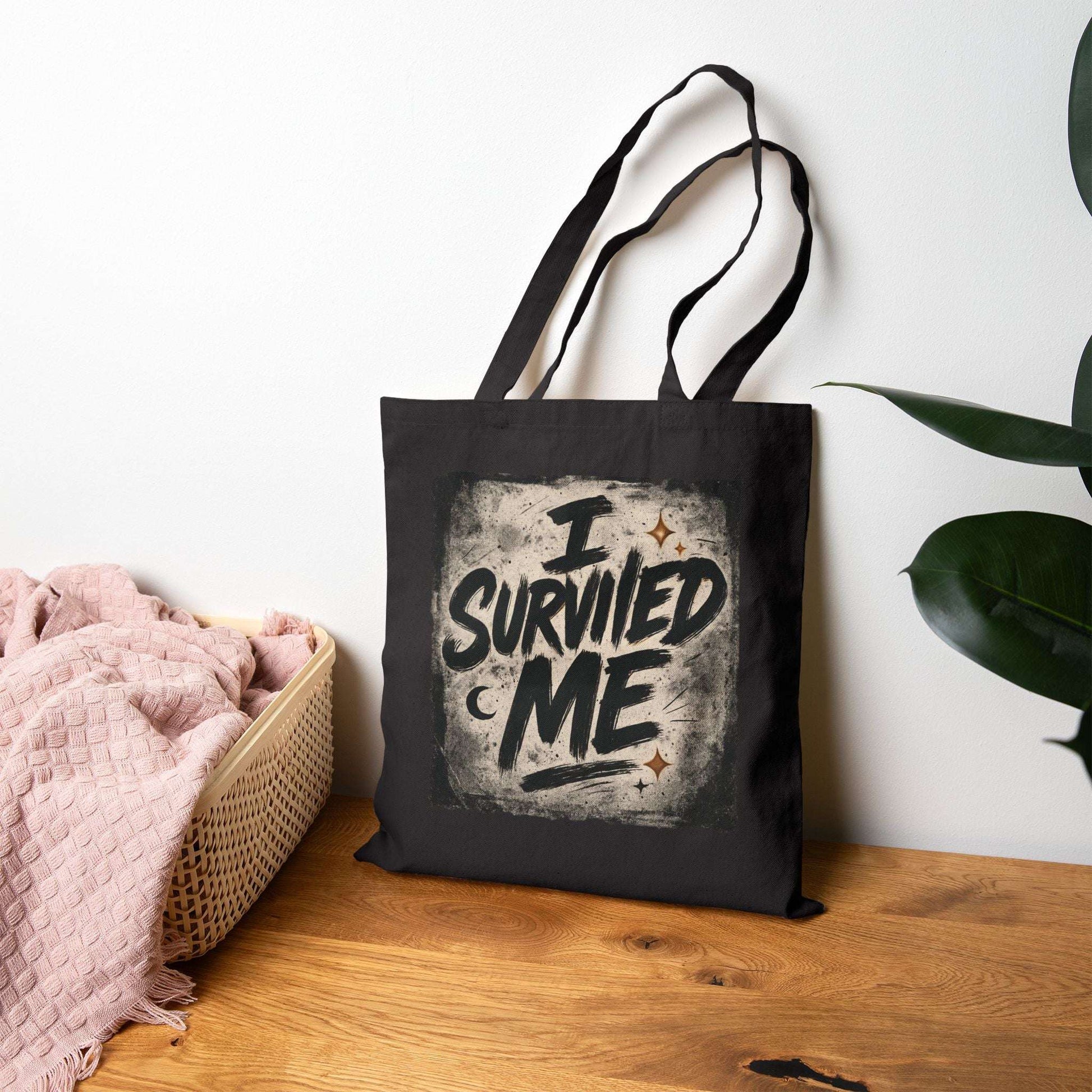 Black canvas tote bag with 'I Survived Me' message placed beside a cozy basket, ideal for therapy survivors and motivational gifting.